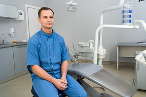 handsome young dentist sitting in dentist office and looking at camera