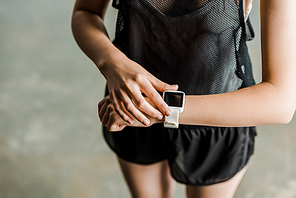 partial view of sportswoman adjusting sport smartwatch with blank screen at gym