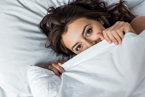 beautiful happy woman hiding under white blanket on bed