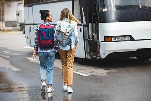 rear view of women with rucksacks walking near travel bus at urban street