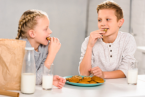happy children eating cookies and drinking milk at table in kitchen