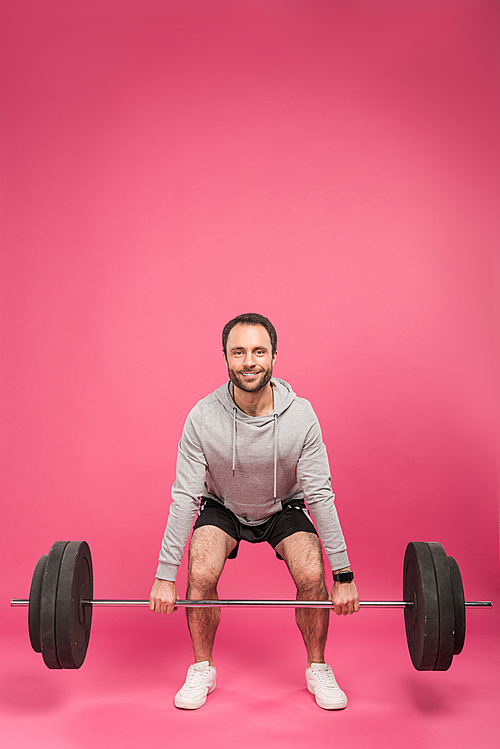 handsome sportsman lifting barbell, isolated on pink