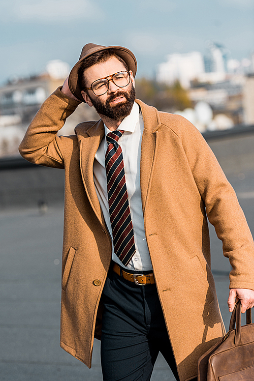 adult bearded businessman walking on roof and touching hat
