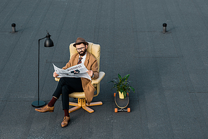 handsome businessman sitting in armchair and reading newspaper on roof