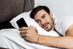 handsome bearded man lying in bed and using smartphone