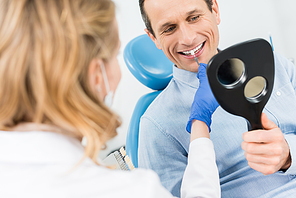 Man choosing tooth implant looking at mirror in modern dental clinic