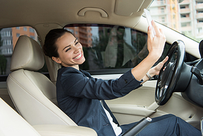 attractive smiling driver taking selfie with smartphone in car