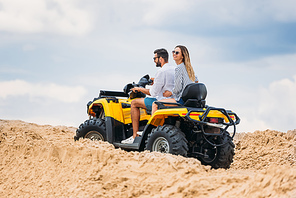 active young couple riding all-terrain vehicle in desert on cloudy day