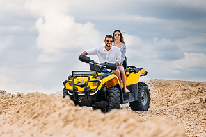 active young couple riding all-terrain vehicle in desert on cloudy day