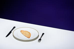 close up view of unhealthy meat pastry on plate and cutlery on table on blue background