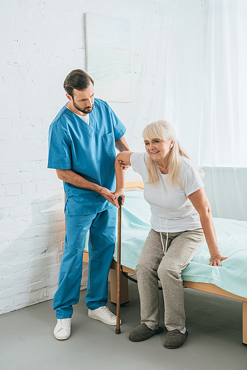 male nurse helping senior woman with walking stick