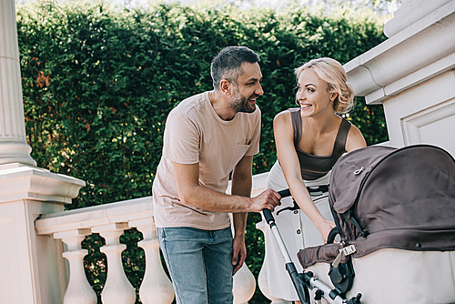 happy parents looking at each other near baby carriage in park