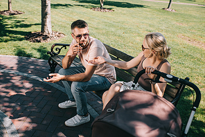 high angle view of husband smoking cigarette near baby carriage in park, wife gesturing and looking at him