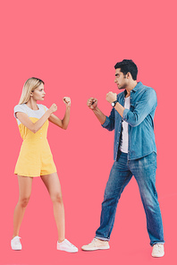 side view of young couple standing in fight position and looking at each other isolated on pink