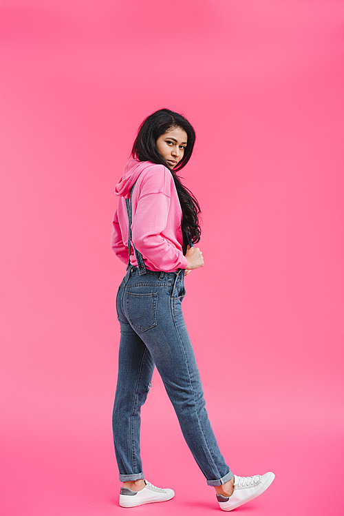 stylish young african american woman in denim overall posing on pink background
