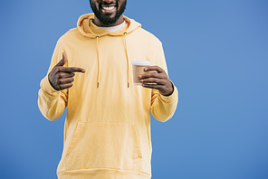 partial view of young african american man pointing by finger at disposable coffee cup isolated on blue background