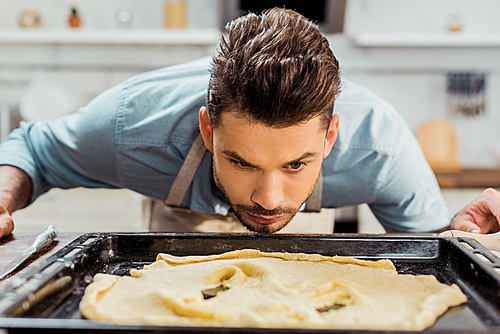 young man in apron looking at spoiled dough on baking tray