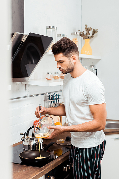 handsome young man in pajamas cooking omelette in frying pan