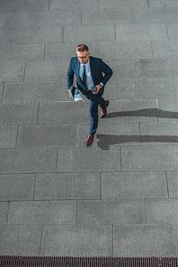 high angle view of businessman with paper cup and newspaper walking on street