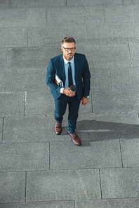 high angle view of handsome middle aged businessman holding coffee to go and  on street