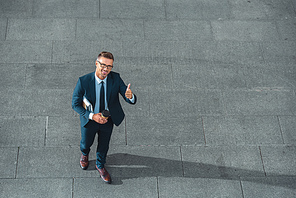 high angle view of happy businessman holding paper cup and showing thumb up on street