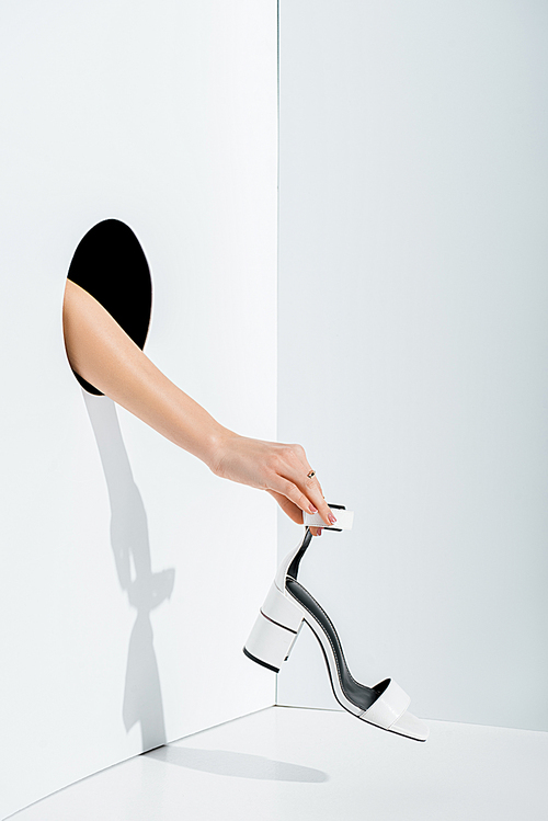 cropped image of girl holding white high heel in hand through hole on white