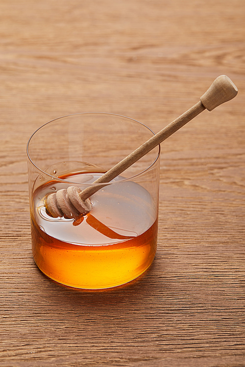 viscous organic honey in glass with stick on wooden table