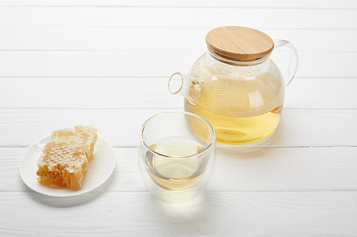 teapot with organic herbal tea, glass and honeycomb on white wooden table