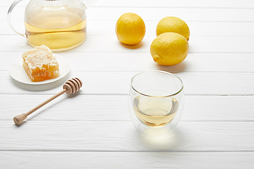 transparent teapot and glass with green tea, lemons, honey dripper and honeycomb on white wooden table
