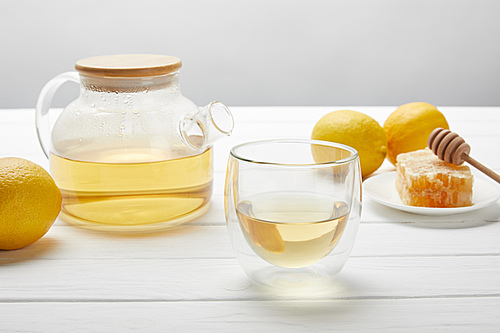 teapot with organic herbal tea, glass, fresh lemons and honeycomb on white wooden table