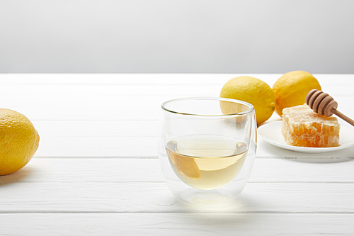 transparent glass with green tea, lemons and honeycomb on white wooden table