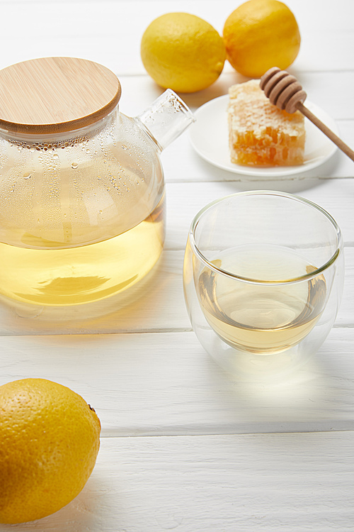 transparent teapot with green tea, fresh lemons and honeycomb on white wooden table