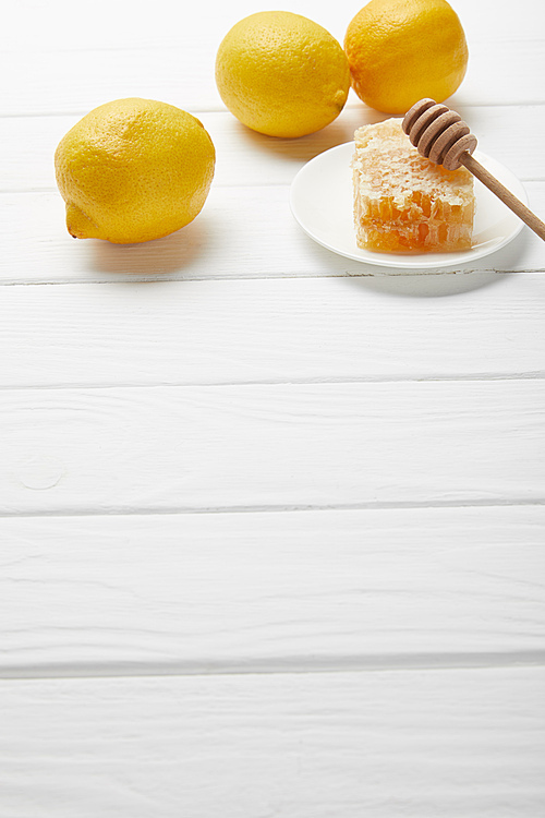 honeycomb and honey dripper on plate with lemons on white wooden table with copy space