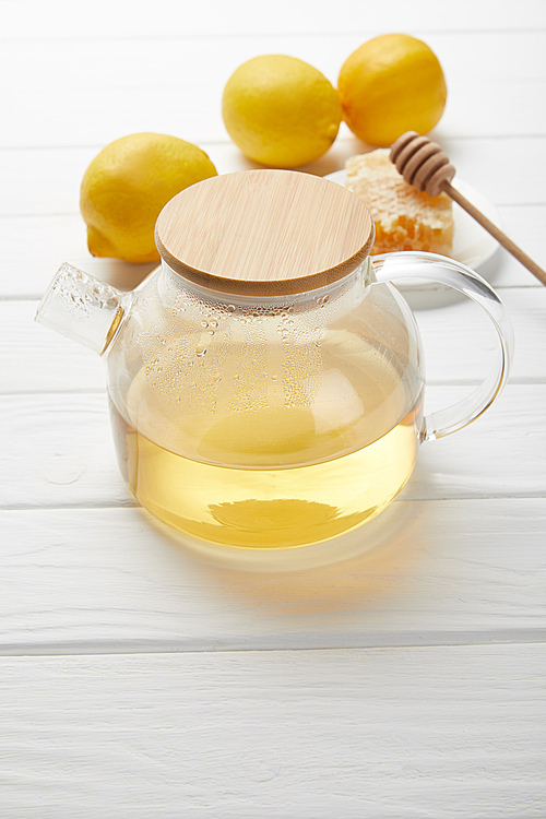 transparent teapot with green tea, lemons and honeycomb on white wooden table