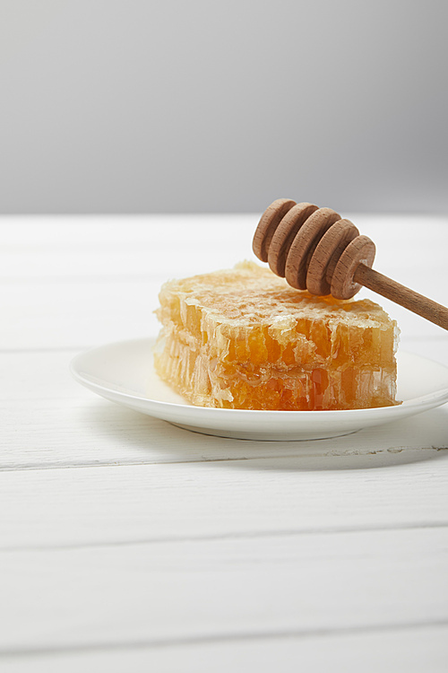plate with honey dripper and delicious honeycomb on white wooden table isolated on grey