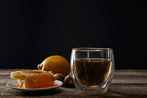 transparent glass with blooming tea, honeycomb and lemon on wooden table isolated on black