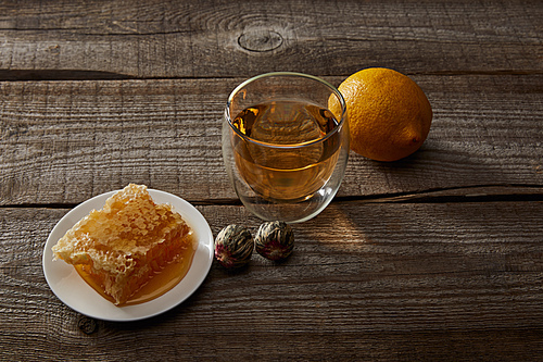 glass of traditional chinese blooming tea, lemon and honeycomb on wooden surface