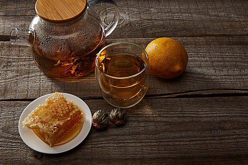 lemon, honeycomb and transparent teapot with glass of chinese blooming tea on wooden table