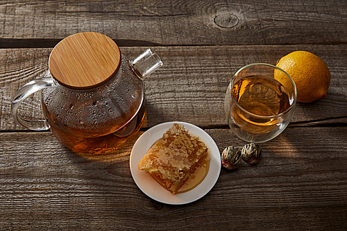 lemon, honeycomb and transparent teapot with glass of chinese blooming tea on wooden table