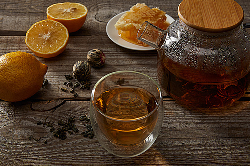 lemons, honeycomb and transparent teapot with glass of chinese blooming tea on wooden surface