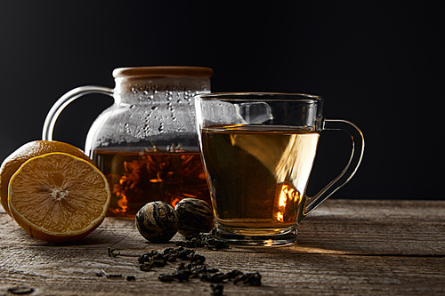 transparent teapot and cup with traditional blooming tea on wooden table with lemons isolated on black