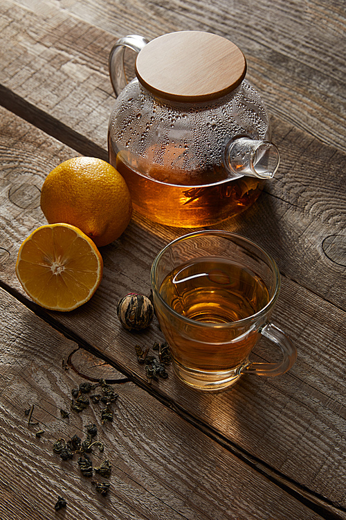 transparent teapot with cup of traditional chinese blooming tea and lemons on wooden surface