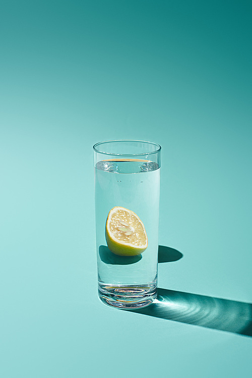 transparent glass with fresh water and lemon on turquoise background