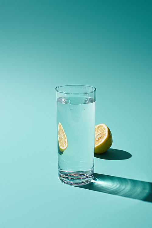 transparent glass with fresh water and lemon half on turquoise background