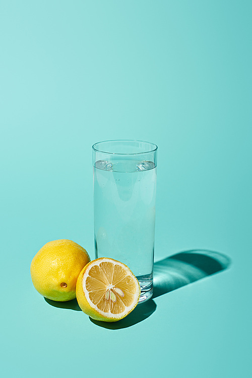 transparent glass with fresh water and bright lemon on turquoise background