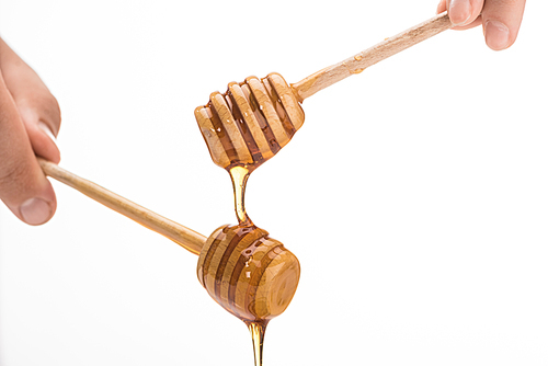 cropped view of man holding wooden honey dippers with dripping honey isolated on white