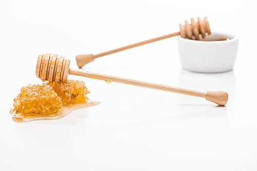 selective focus of honeycomb with sweet honey and wooden honey dippers isolated on white