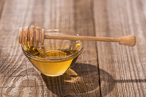 glass bowl with tasty honey and honey dipper on wooden table in sunlight