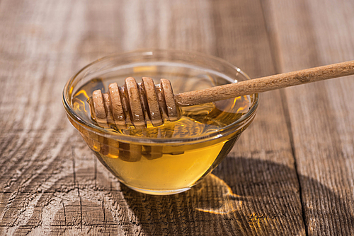 glass bowl with delicious honey and honey dipper on wooden table in sunlight