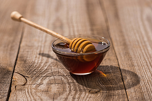 glass bowl with honey and honey dipper on wooden table in sunlight